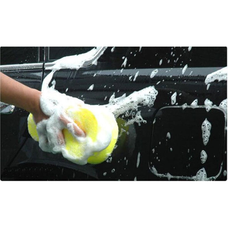Hand scrubbing a car with a yellow porous sponge, foamy bubbles visible