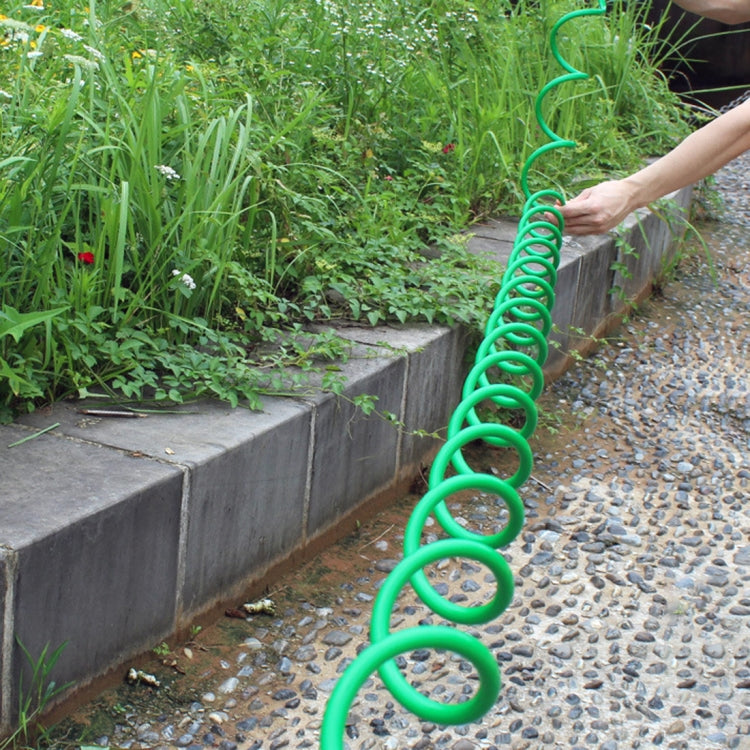 Green spiral hose extended along garden walkway beside plants and stone border