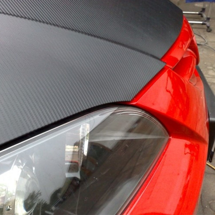Close-up of black carbon fiber vinyl wrap edge on car near headlight area