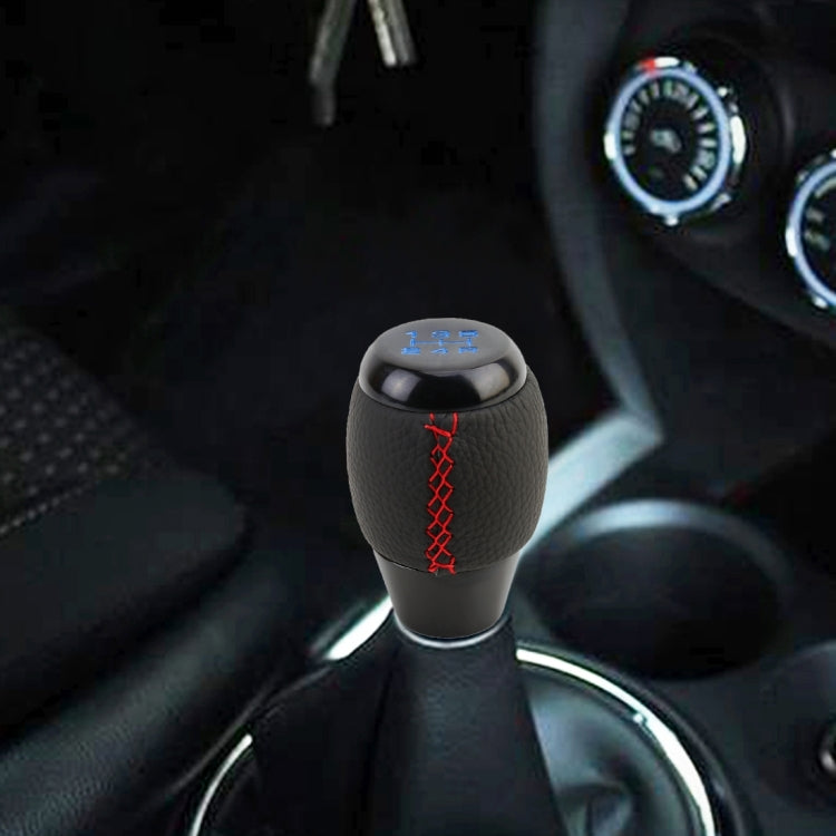 Black leather shift knob with red stitching and blue gear markings, side view.