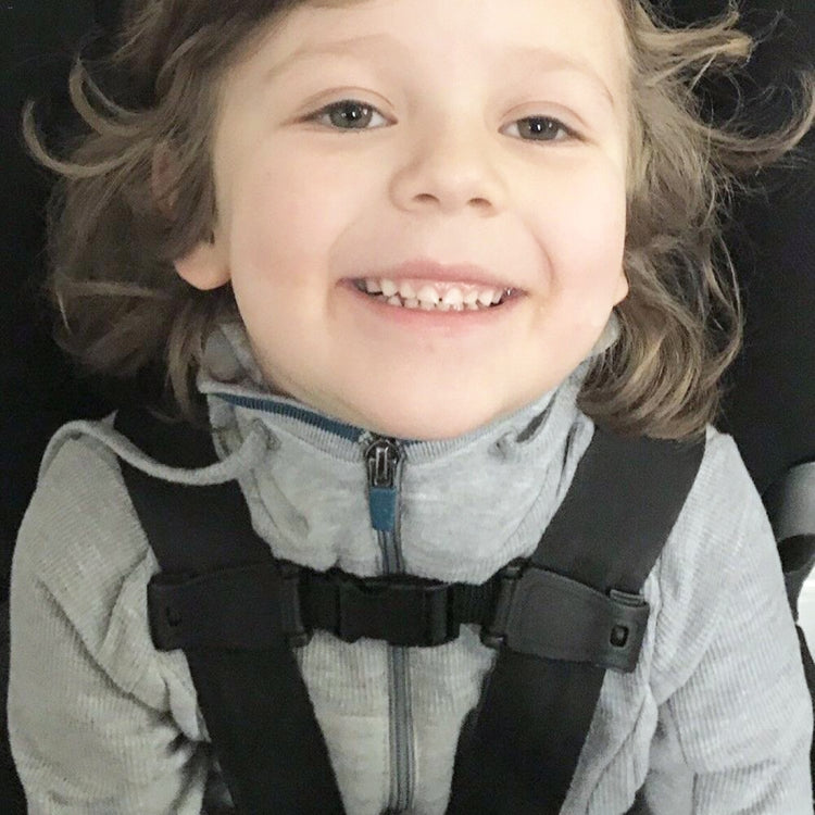 Child wearing a gray seat belt harness with shoulder straps and dark adjuster buckle