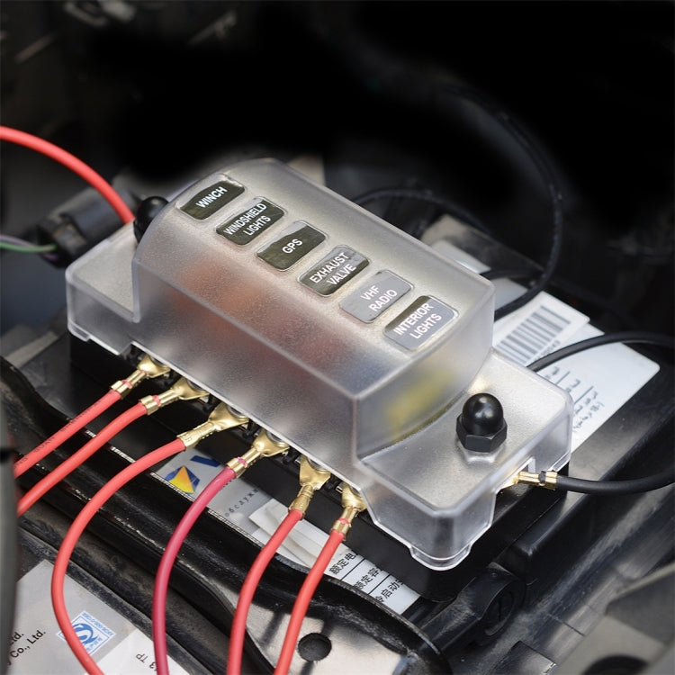 Installed auto fuse box with silver cover and screw terminals, connected with red wires