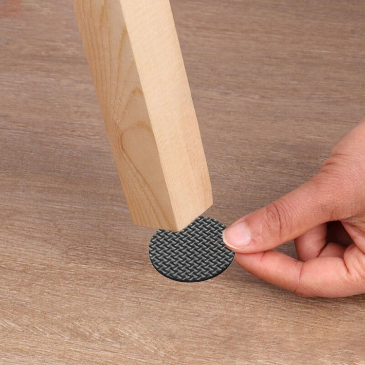 Hand pressing a round dark gray textured foot pad onto a wooden furniture leg