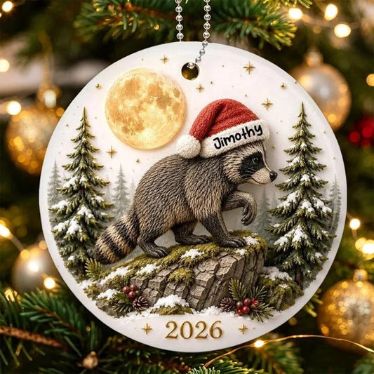 Round hanging raccoon ornament showing Jimothy on a rock with pine trees, '2026'.