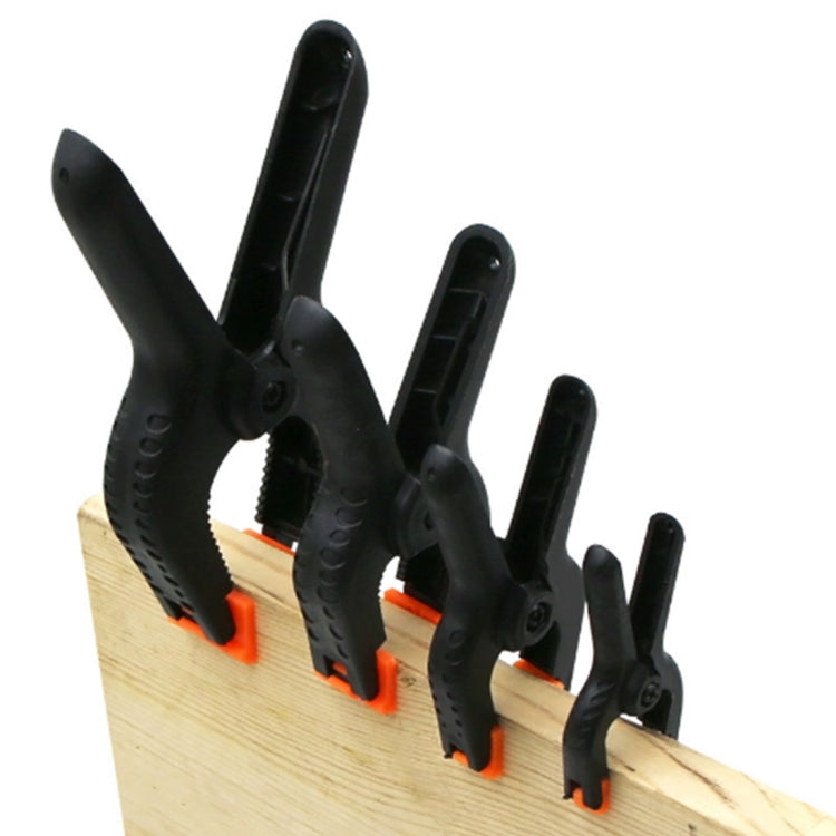 Set of black spring clamps with orange tips holding a wooden board edge.