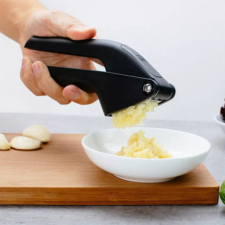 Hand pressing garlic with a black garlic presser over a bowl of minced garlic