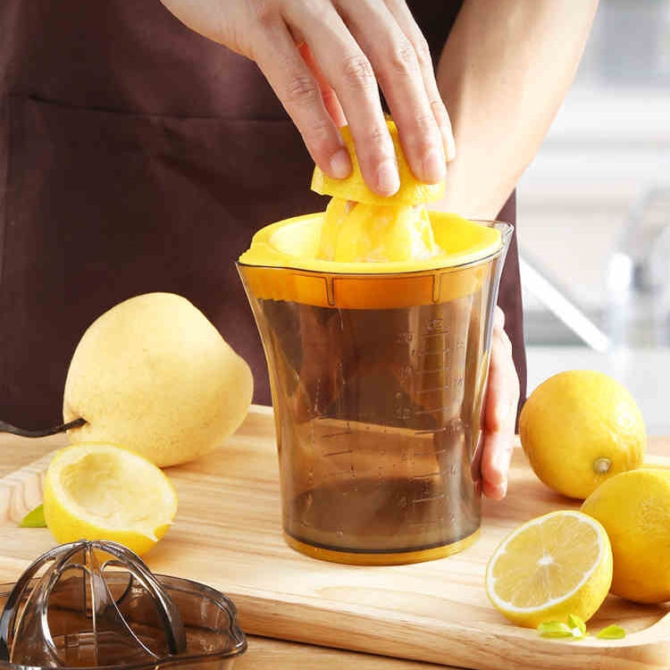 Manual citrus juicer with yellow press cone and amber container, lemon being squeezed