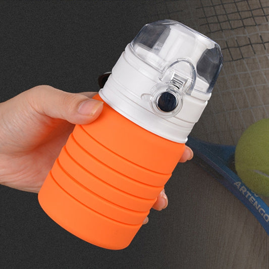 Orange collapsible silicone cup with clear lid, held in hand near a metal surface.