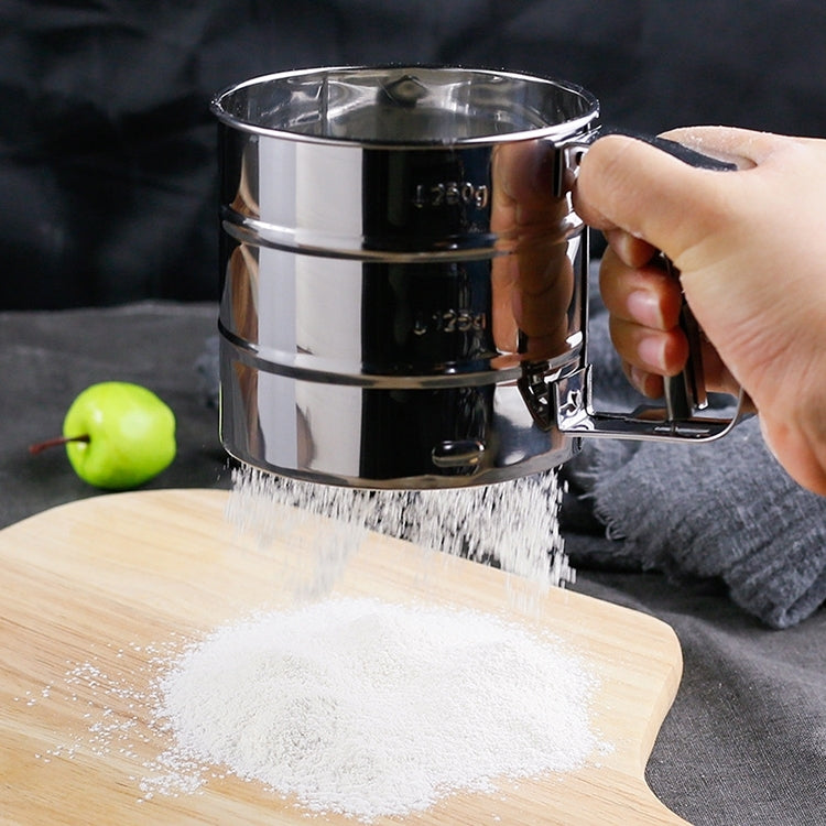 Handheld stainless steel sifter pouring flour from mesh screen onto wooden board