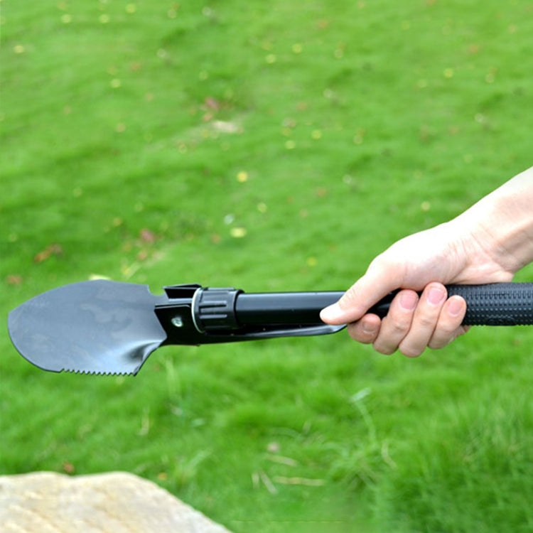 Hand holding folding camping shovel with extended spade blade for digging