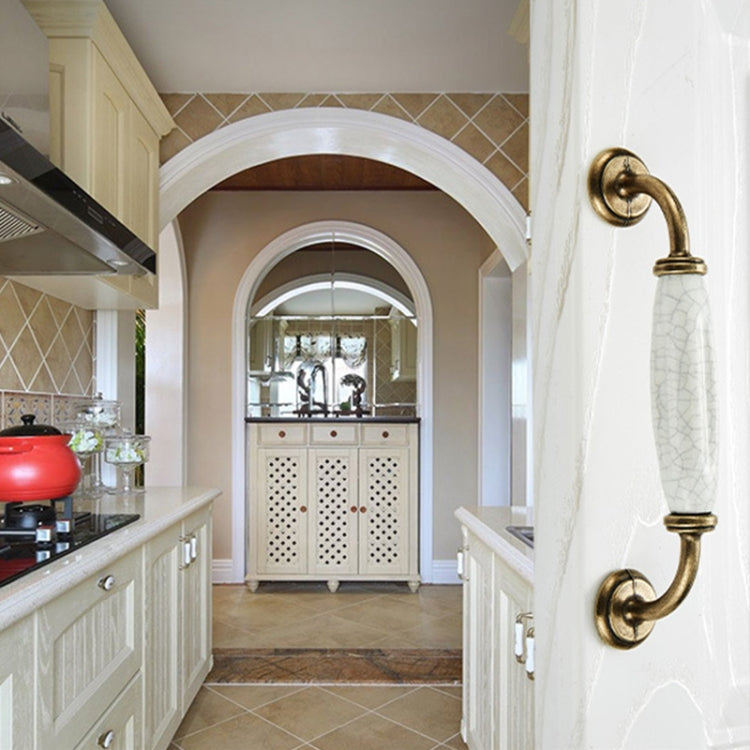 Ceramic crackle cabinet handle with antique brass curved pull on a white door panel