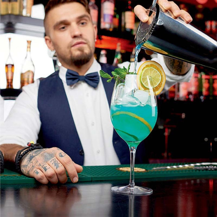 Stainless steel shaker pouring cocktail into stem glass on bar counter