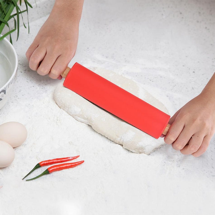 Red silicone rolling pin with wooden handles, held by hands over dough log.