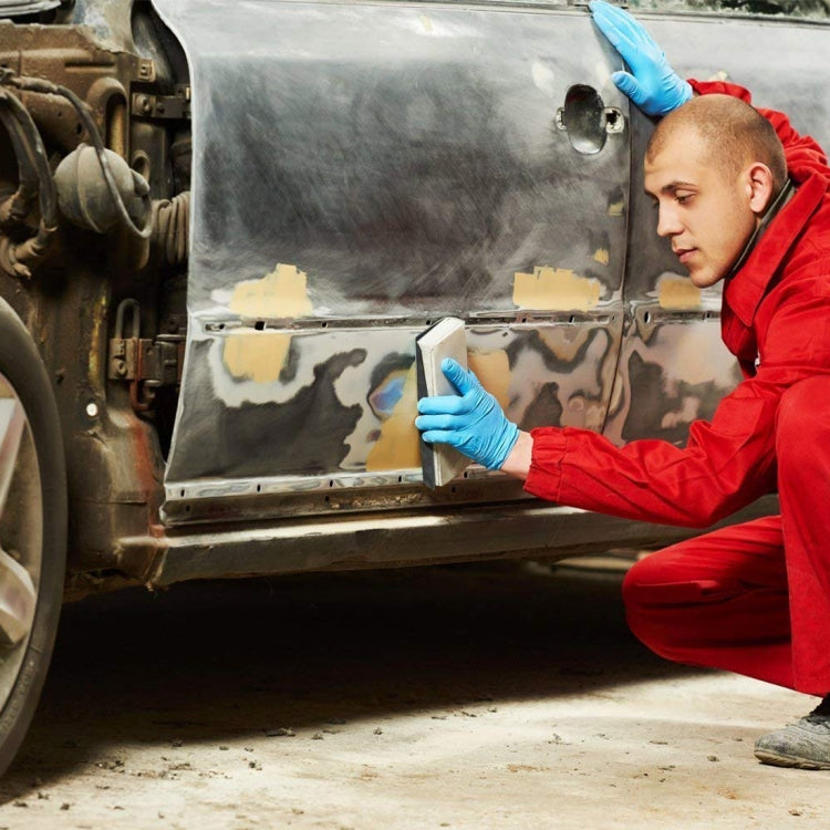 Auto detailing worker in red jacket wearing blue gloves sanding a vehicle panel