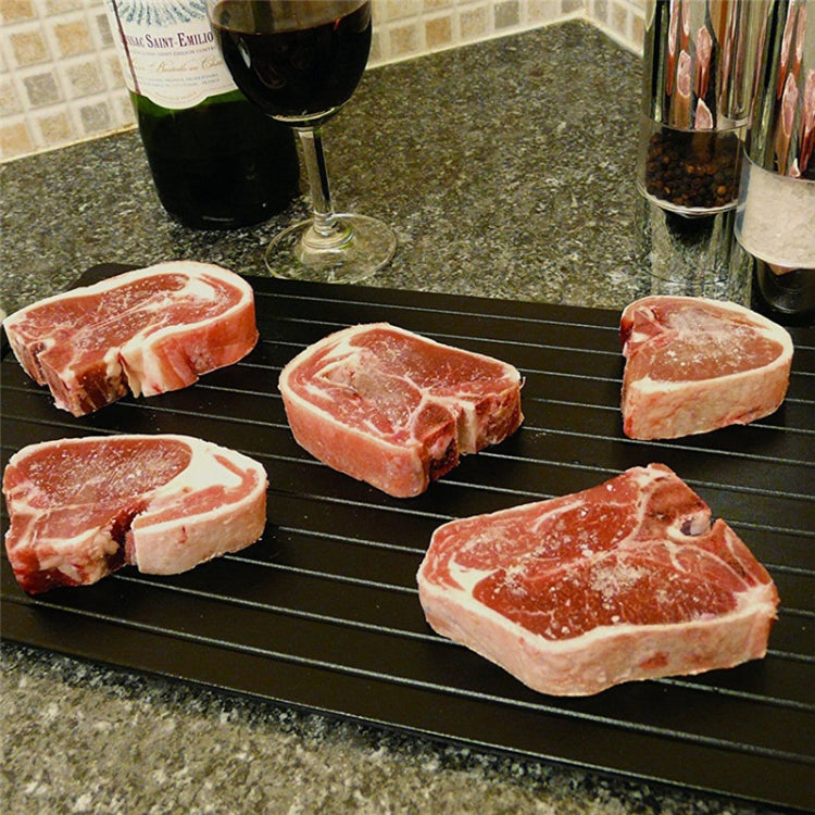 Black ribbed rapid defrosting tray with several raw meat chops on counter