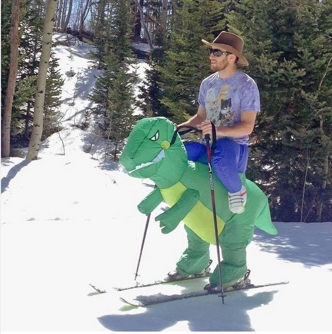 Green inflatable dinosaur costume on skier with backpack-style battery pack
