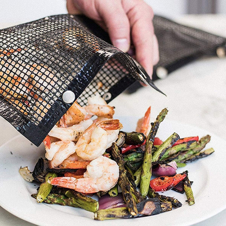 Hand tilting black grilling mesh BBQ bag onto a plate of grilled food.