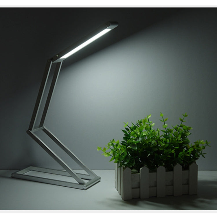 Silver LED desk lamp casting bright bar light from folding stand