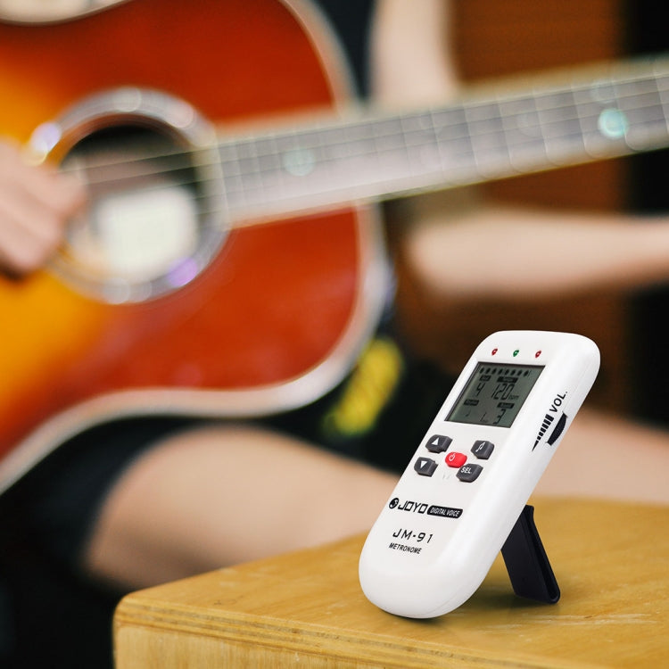 White mini electronic vocal metronome/tuner placed on wood near an acoustic guitar