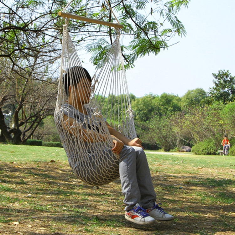 Rope net hammock swing with a seated person, suspended outdoors from trees