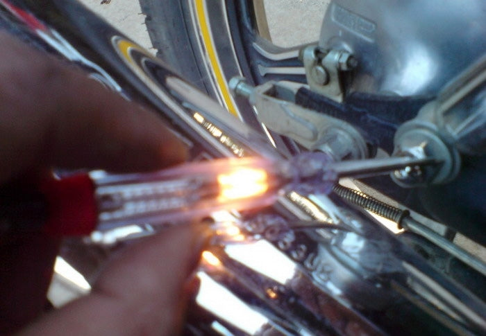 Hand using car voltage tester probe near vehicle wiring