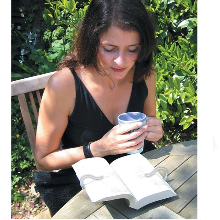 White hands-free reading book holder holding an open book on a table outdoors