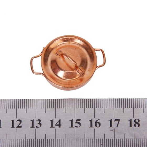 Miniature copper pot with lid and loop handles, next to ruler for size
