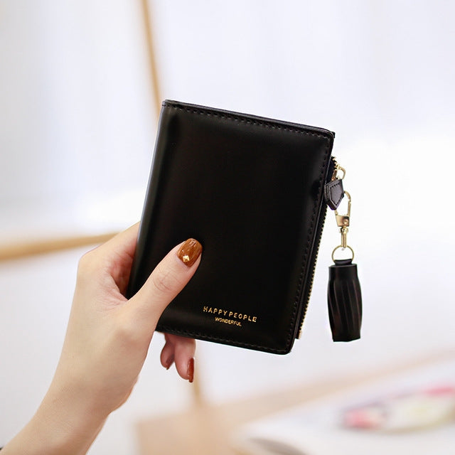 Black women’s bifold wallet with tassel keychain and gold hardware, held in hand