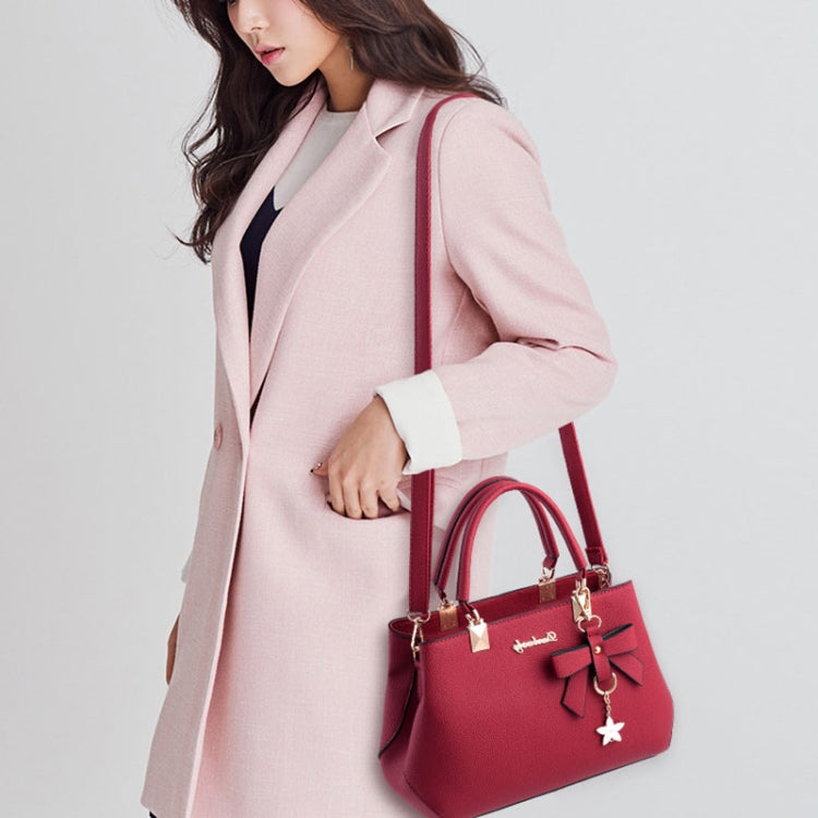 Women's burgundy tote bag with star charm, carried with top handles