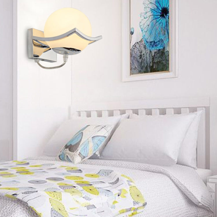 Wall-mounted globe glass lamp glowing beside bed with round frosted shade and arm