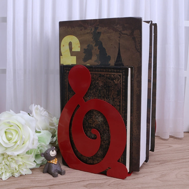 Red musical-note metal bookend standing beside stacked books on floor