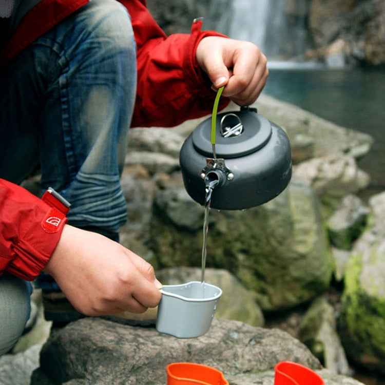 Portable aluminum kettle pouring hot water outdoors into a small cup