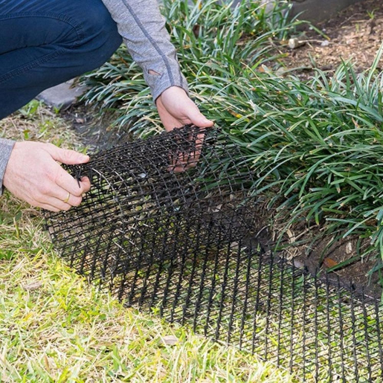 Black wire mesh barrier mat being installed with hands in grass