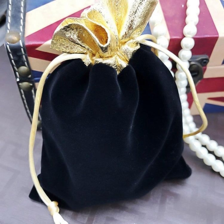 Black velvet drawstring jewelry pouch with gold bow and beige pull-cords, pearls nearby