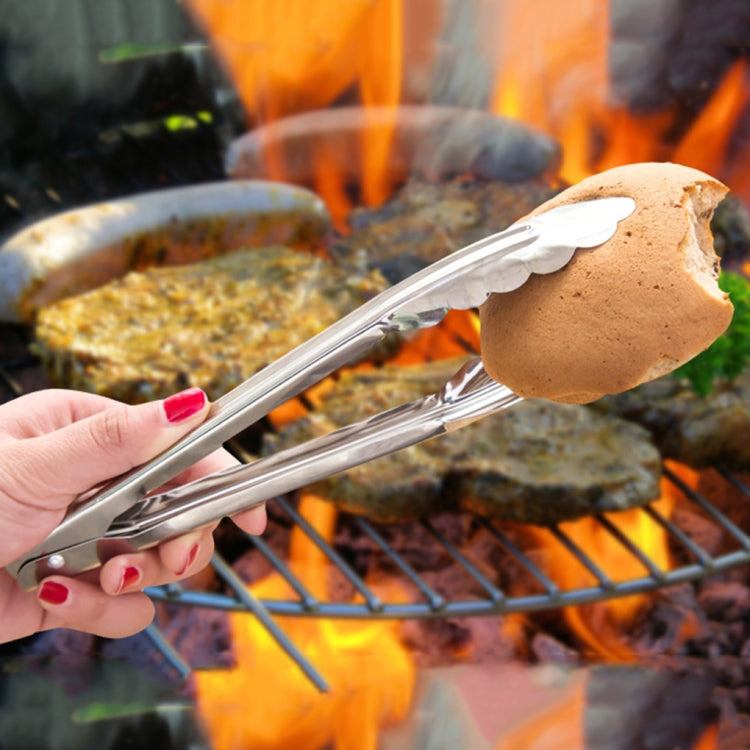 Stainless steel clip holding bread above flames on a grill grate; hand grips handles