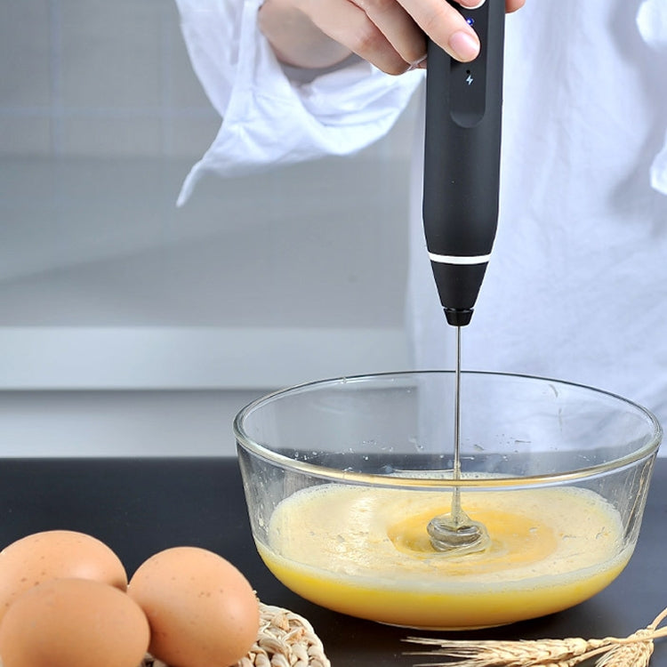 Black hand mixer stirring batter in a glass bowl with whisk attachment