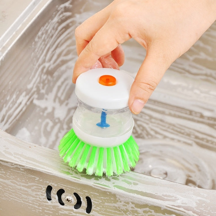 Kitchen sink scrub brush with green bristles and clear soap dispenser with orange cap