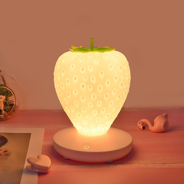 White silicone strawberry LED night light glowing on round base with power icon