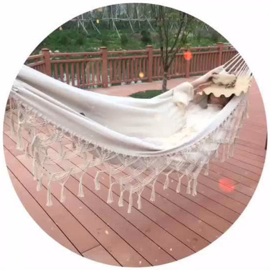 White canvas hammock with fringe trim and hammock fabric drape over a deck