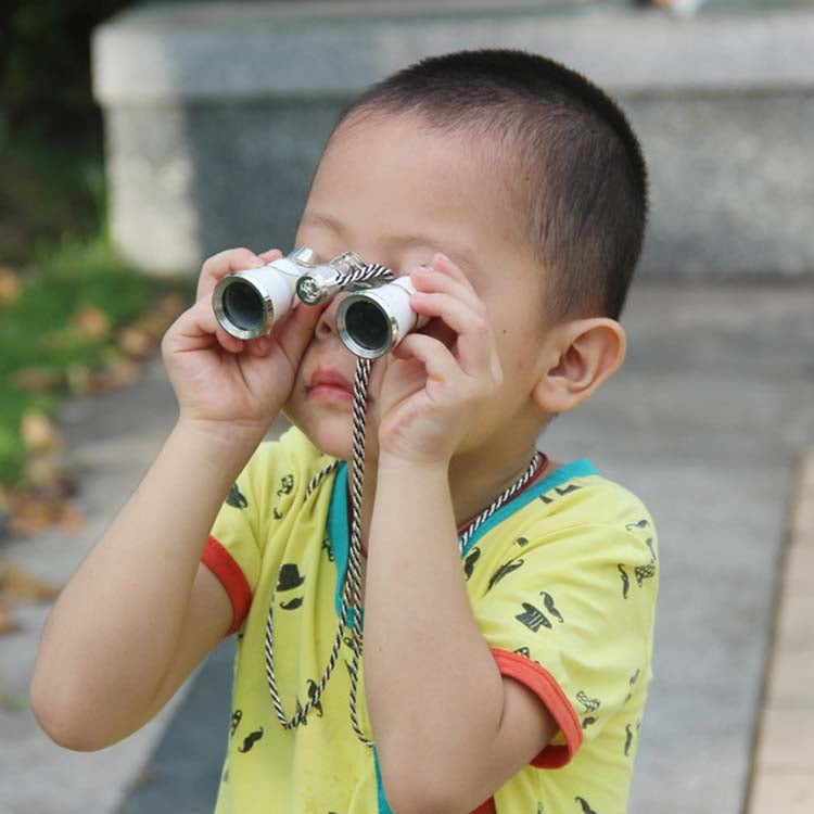 Classical opera binoculars with gold trim and braided chain held to a child's eyes