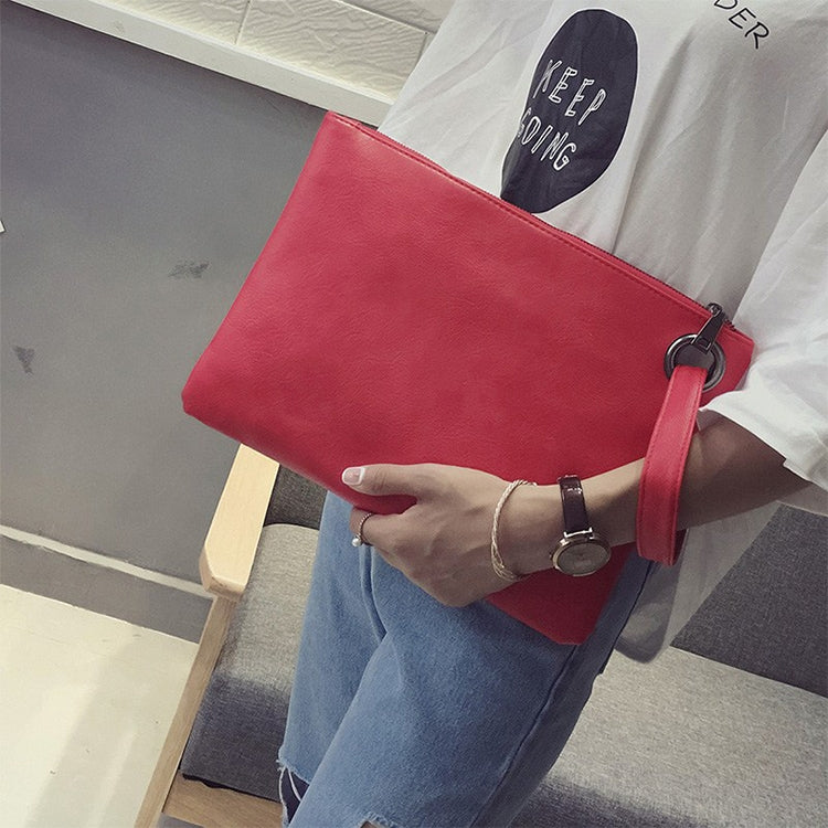 Red zippered envelope clutch bag with wrist strap, held in hand