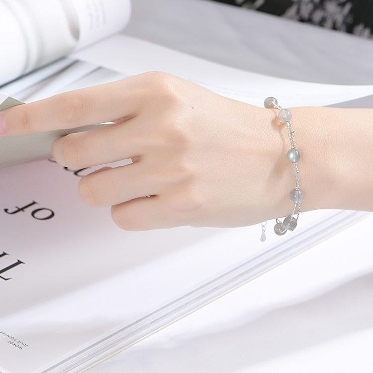 Silver bracelet on wrist with light blue-gray round beads and small dangling charms