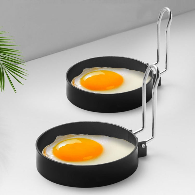 Two round non-stick egg ring molds with long handles holding sunny-side-up eggs