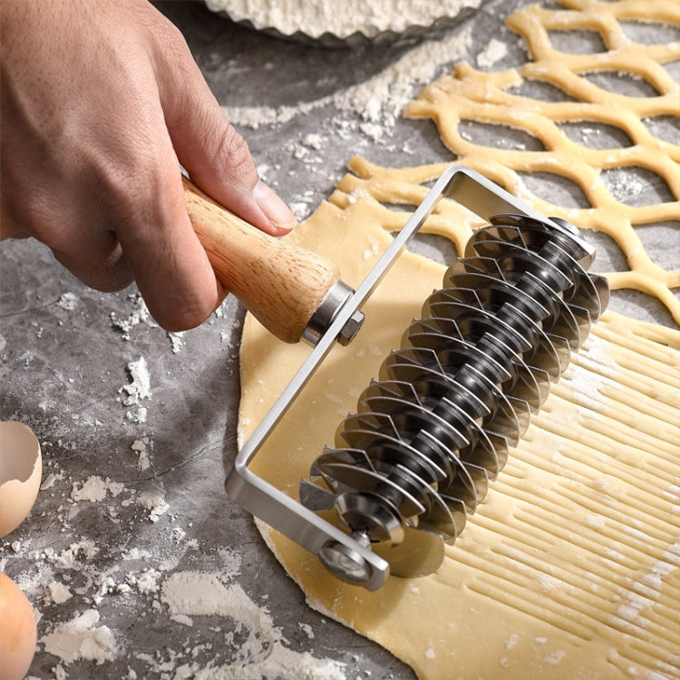 Hand using stainless steel pizza roller cutter on dough, wooden handle grip