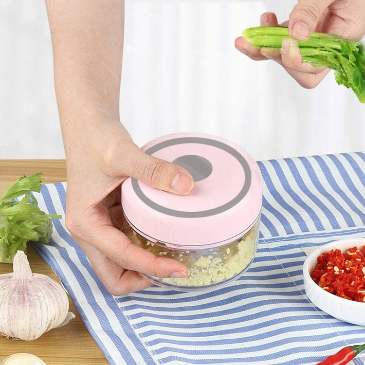 Hand using pink mini garlic masher on garlic cloves with chopped greens
