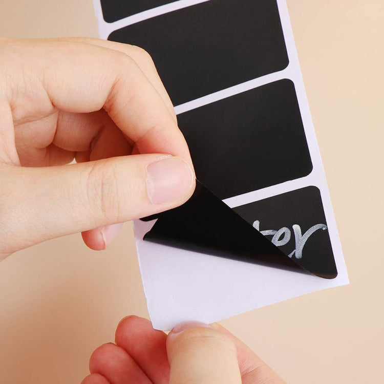 Hand applying dark gray chalkboard label stickers from a white backing sheet