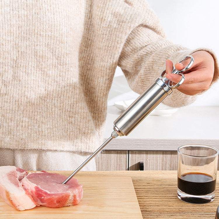Hand using stainless steel seasoning syringe to inject marinade into raw meat