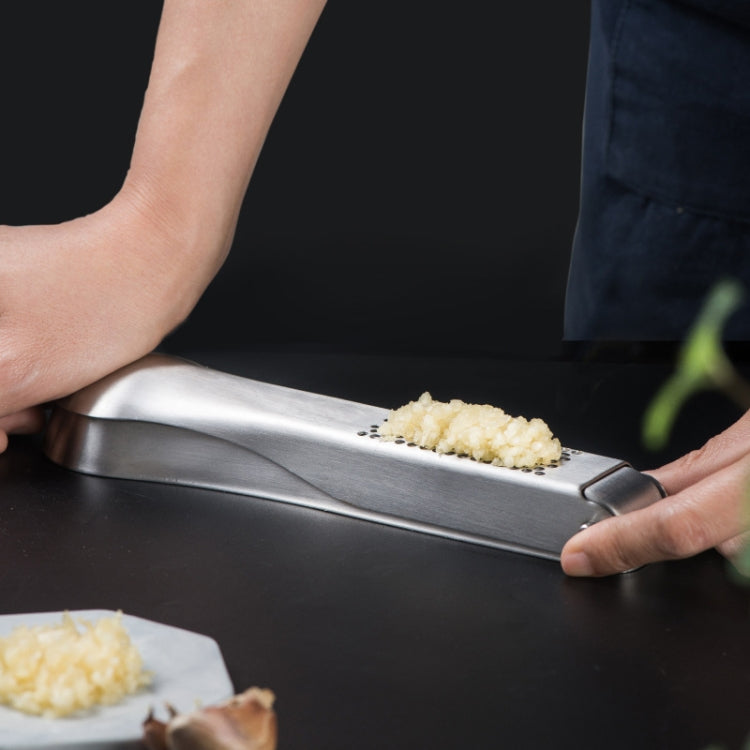 Manual stainless steel garlic masher being used with garlic on the grating plate