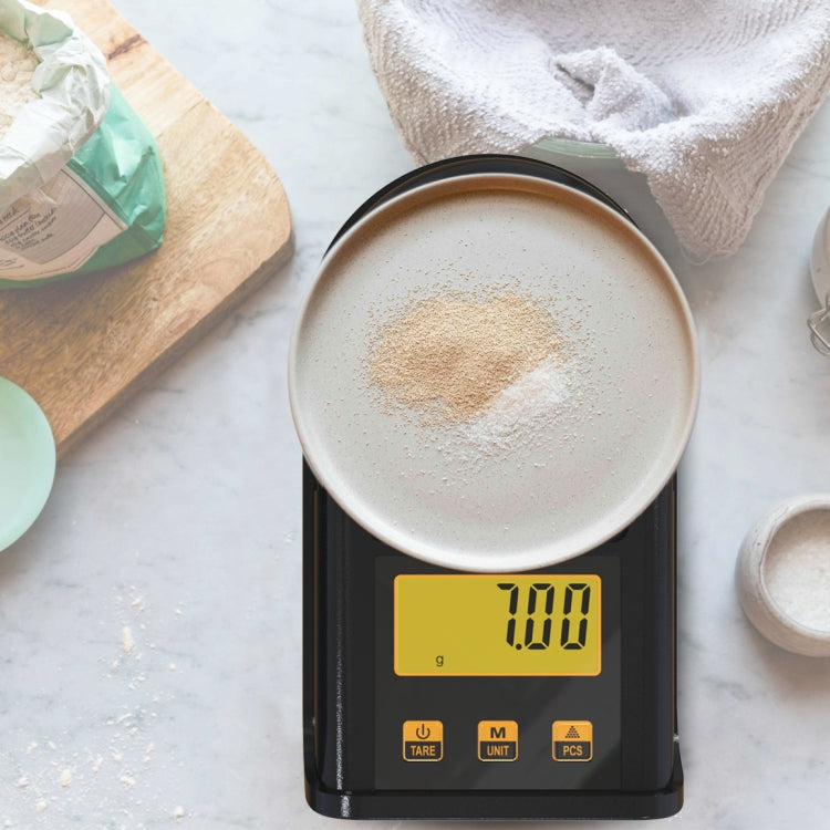 Black digital pocket scale weighing a cup on its metal platform, showing yellow LCD