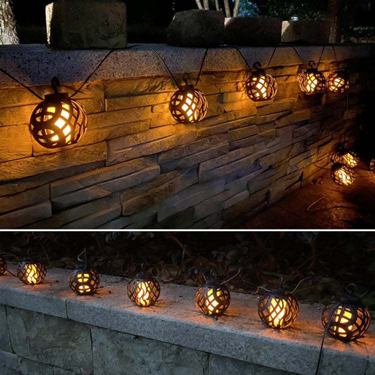 Warm glowing black flame ball solar string lights along a stone wall